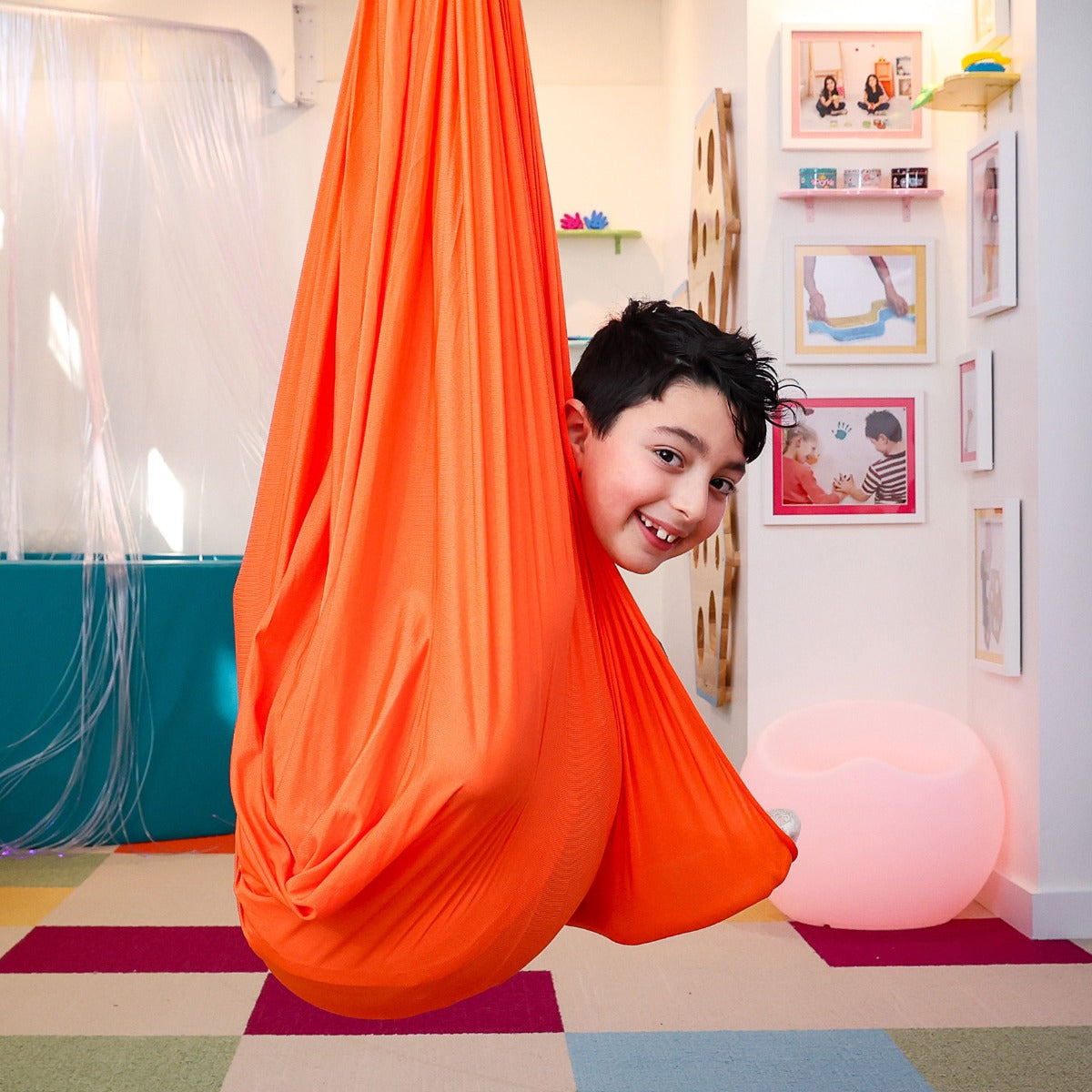 boy peeking out from inside the orange Cozy Compression Swing