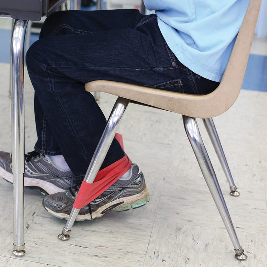 boy using a stretchy red resistance band around the front legs of his chair