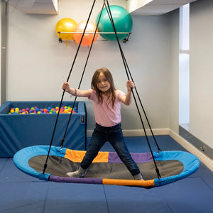 girl standing while swinging indoors on the Magic Carpet Swing