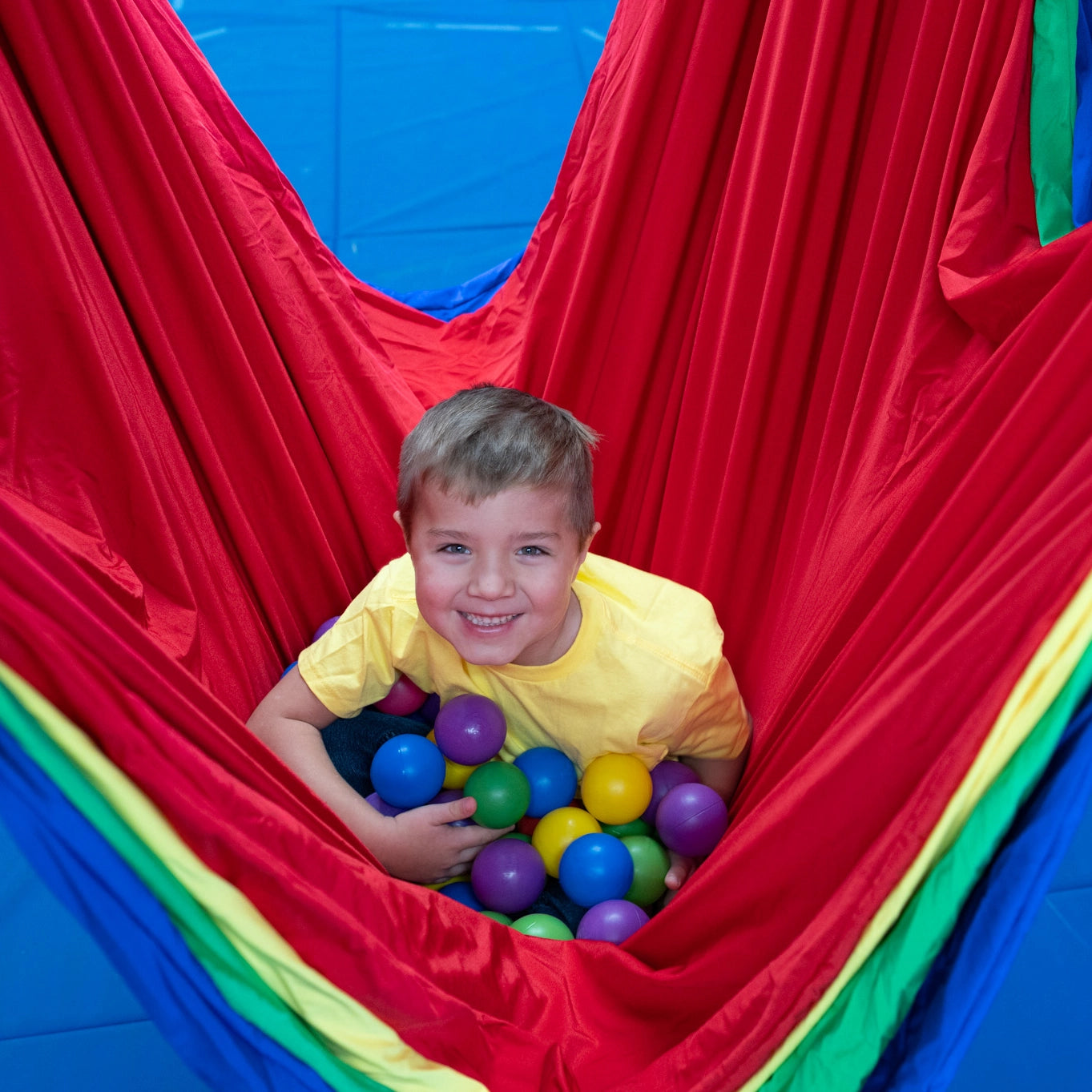 child hugging balls in colorful acrobat hammock swing indoors