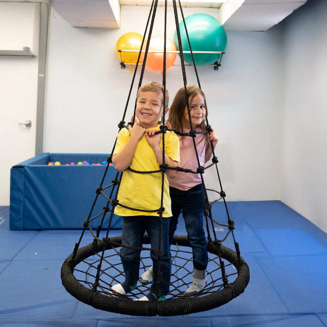 girl and boy smiling while standing on the black Web Tower Swing