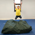 boy indoors swinging and hanging from Trapeze Swing above crash mat
