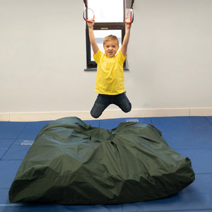 boy indoors swinging and hanging from Trapeze Swing above crash mat