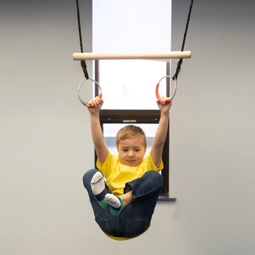 boy indoors with feet up and hanging from Trapeze Swing above crash mat