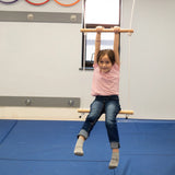 child holding top bar of a double trapeze bar swing while swinging indoors. 