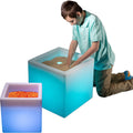 Boy playing with the blue LimeLite™ LED Sand Table with another sand table filled with pebbles near it.