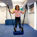 child standing on blue bolster swing indoors