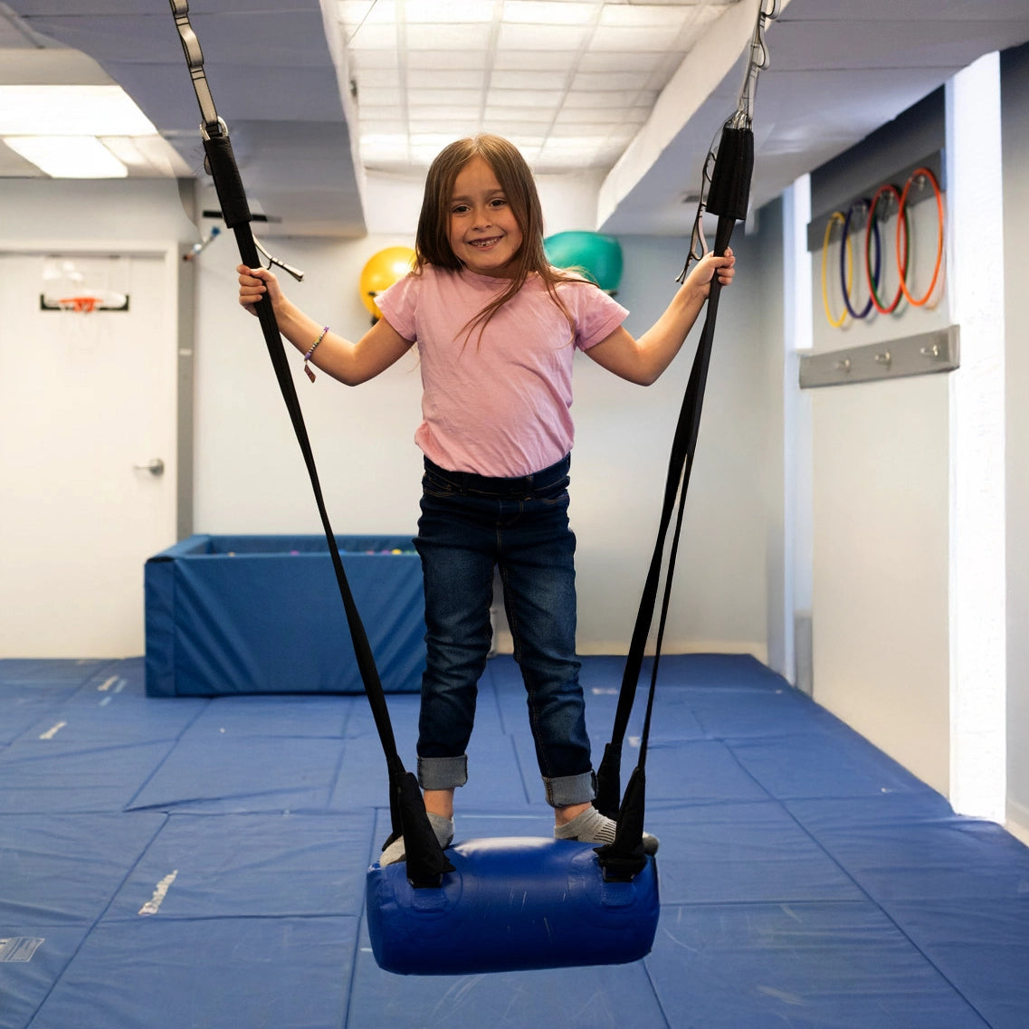 child standing on blue bolster swing indoors