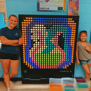 Two girls smiling and standing beside the LiteZilla Light Wall