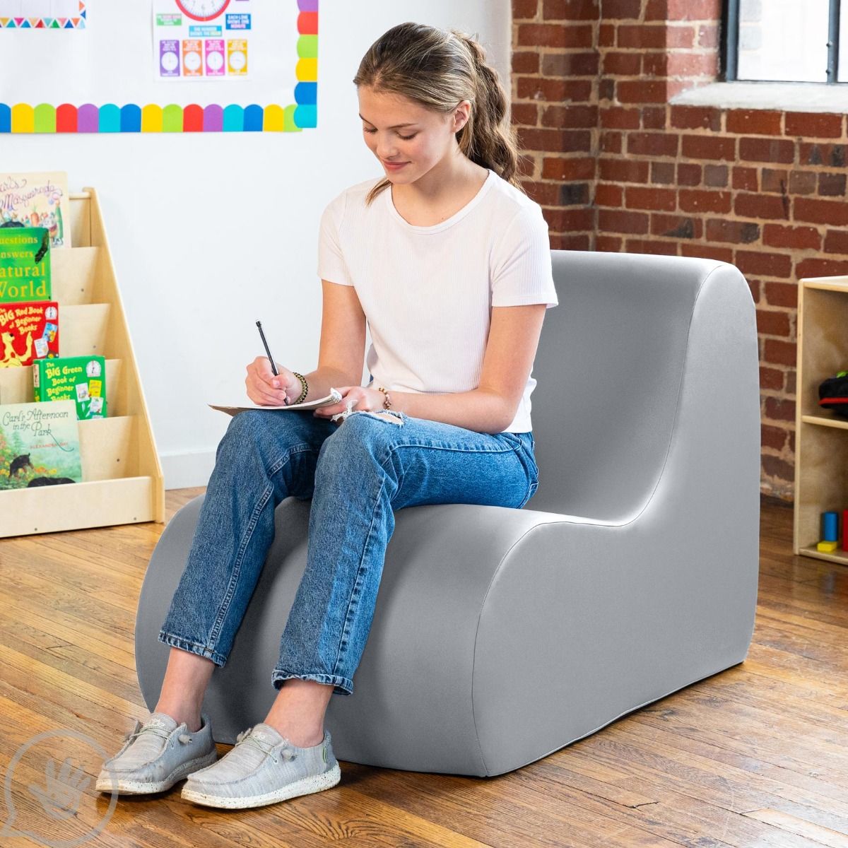 Girl writing notes while sitting on the Sensory Wave Chair in the color gray