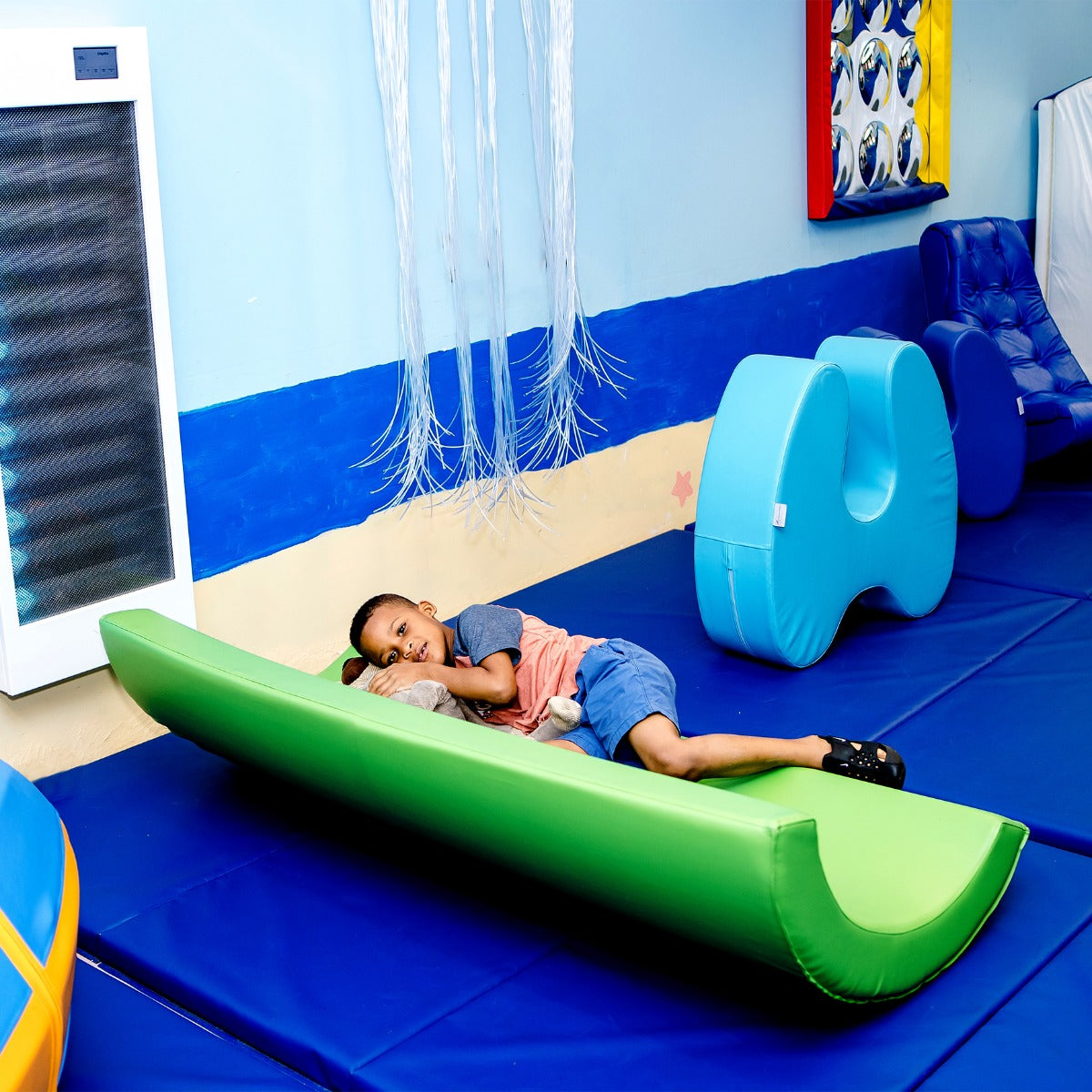 Child smiling while laying on the SensaSoft™ Rocking Half Barrel