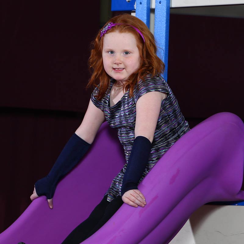 Girl smiling on the slide while wearing the Sensory Sleeves