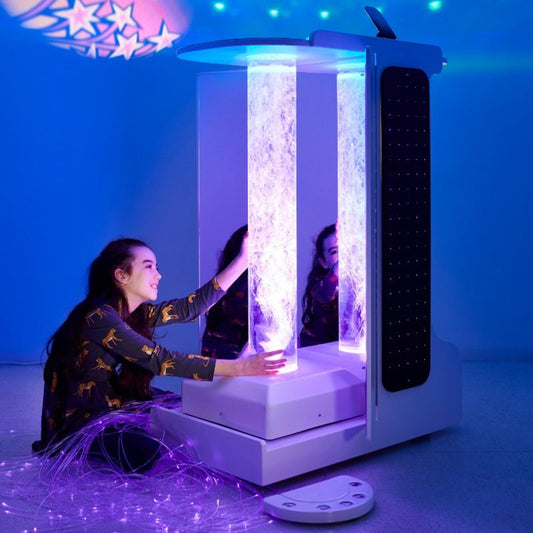 Child smiling while interacting with a brightly lit bubble tube on the Mobile Sensory Cart