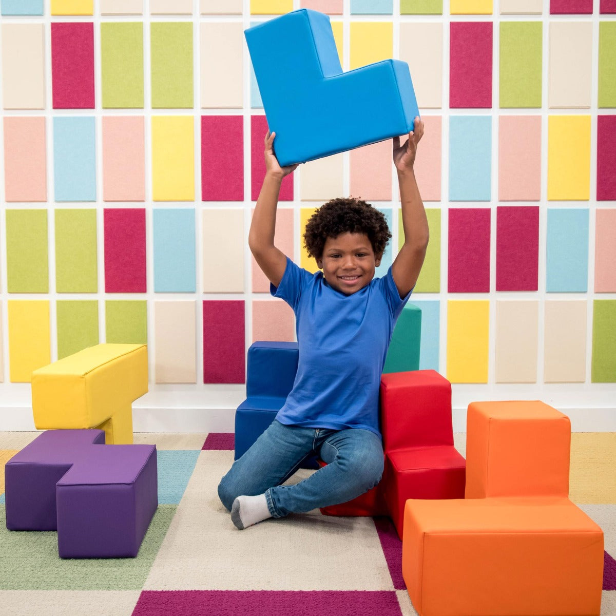 Boy smiling while playing with the SensaSoft Puzzle Cubes, holding a blue cube in the air