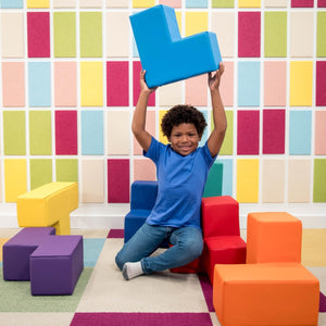 Boy smiling while playing with the SensaSoft Puzzle Cubes, holding a blue cube in the air