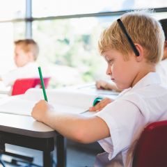 Boy calmly taking notes in the classroom using the HamiltonBuhl Noise Off headset in the color black